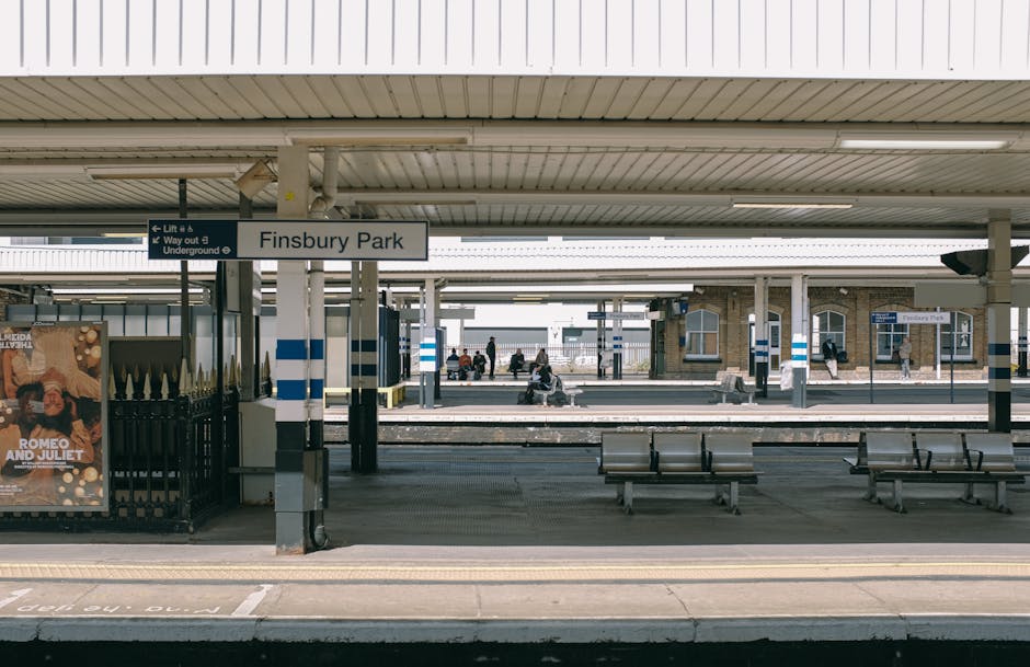 Exterior view of Finsbury Park railway station platform with a white overhead canopy supported by metal columns. A blue and white sign displays 